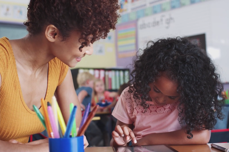 A teacher watches over a student while they are writing