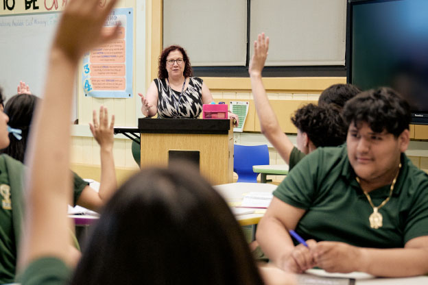 Students and teacher engage, raising hands