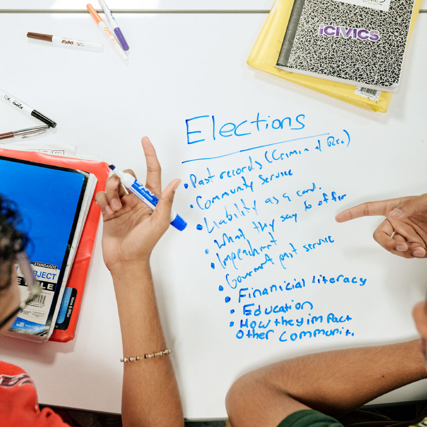 _0023_iCivics_GRC-3192 student hands with marker writing on whiteboard table about elections